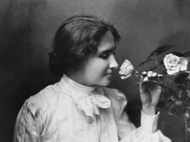 Photo of Helen Keller smelling a rose and smiling.